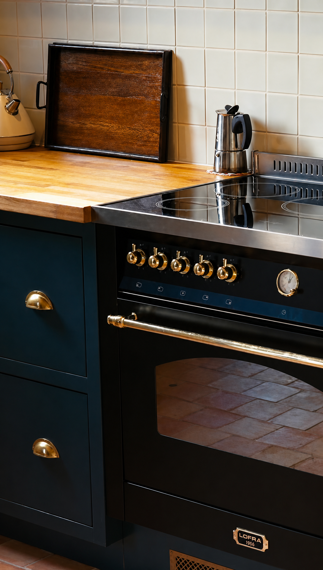 The black range cooker set into dark blue kitchen cabinets with brass cup handles and terracotta floor tiles