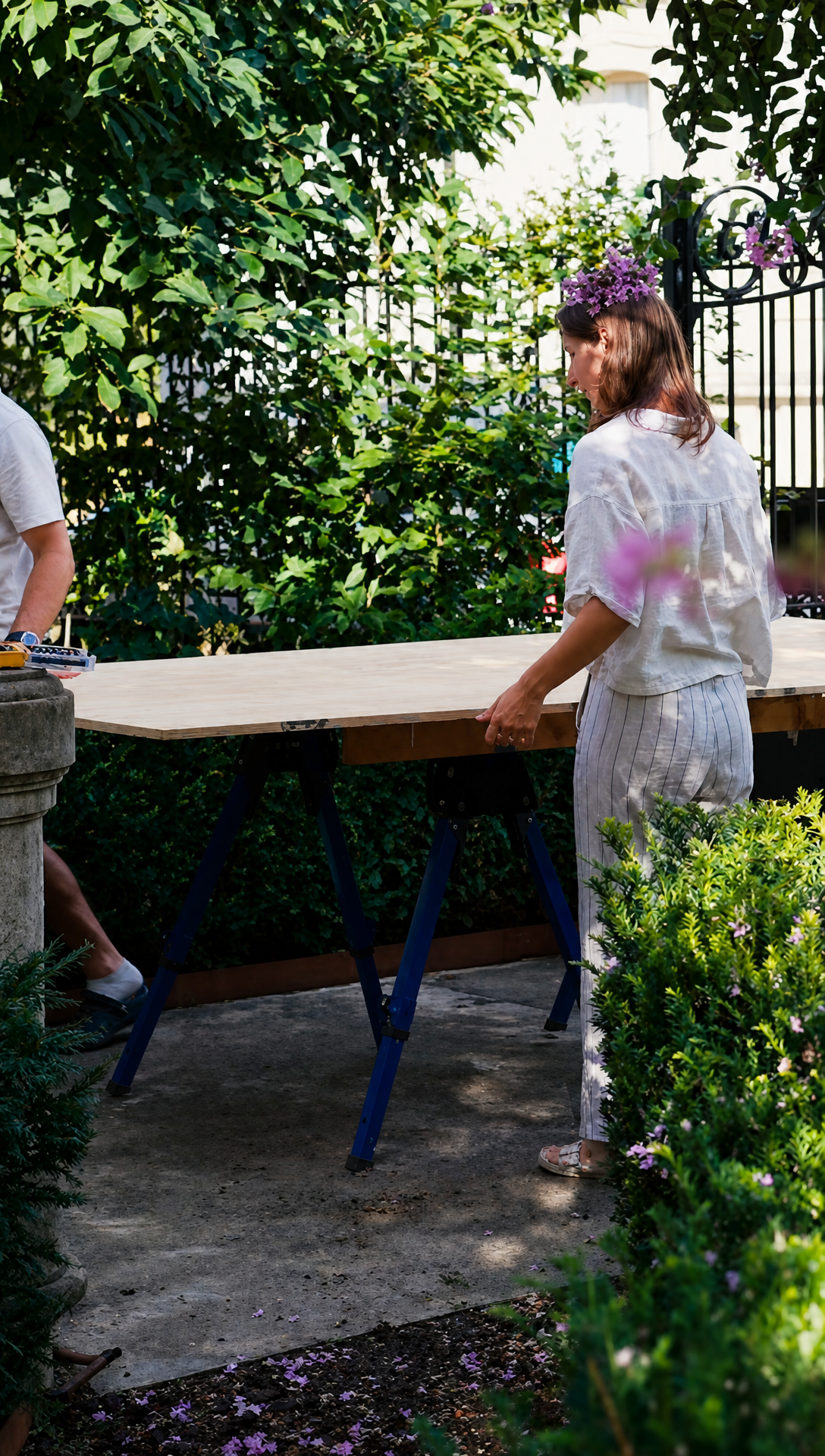 Hugo and Romy laying a large plywood sheet onto sawhorses in the garden by the wrought iron gate