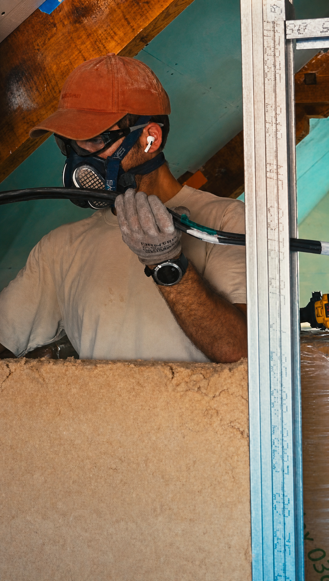 Hugo in a respirator fitting wood fibre insulation between the metal studs of an attic wall
