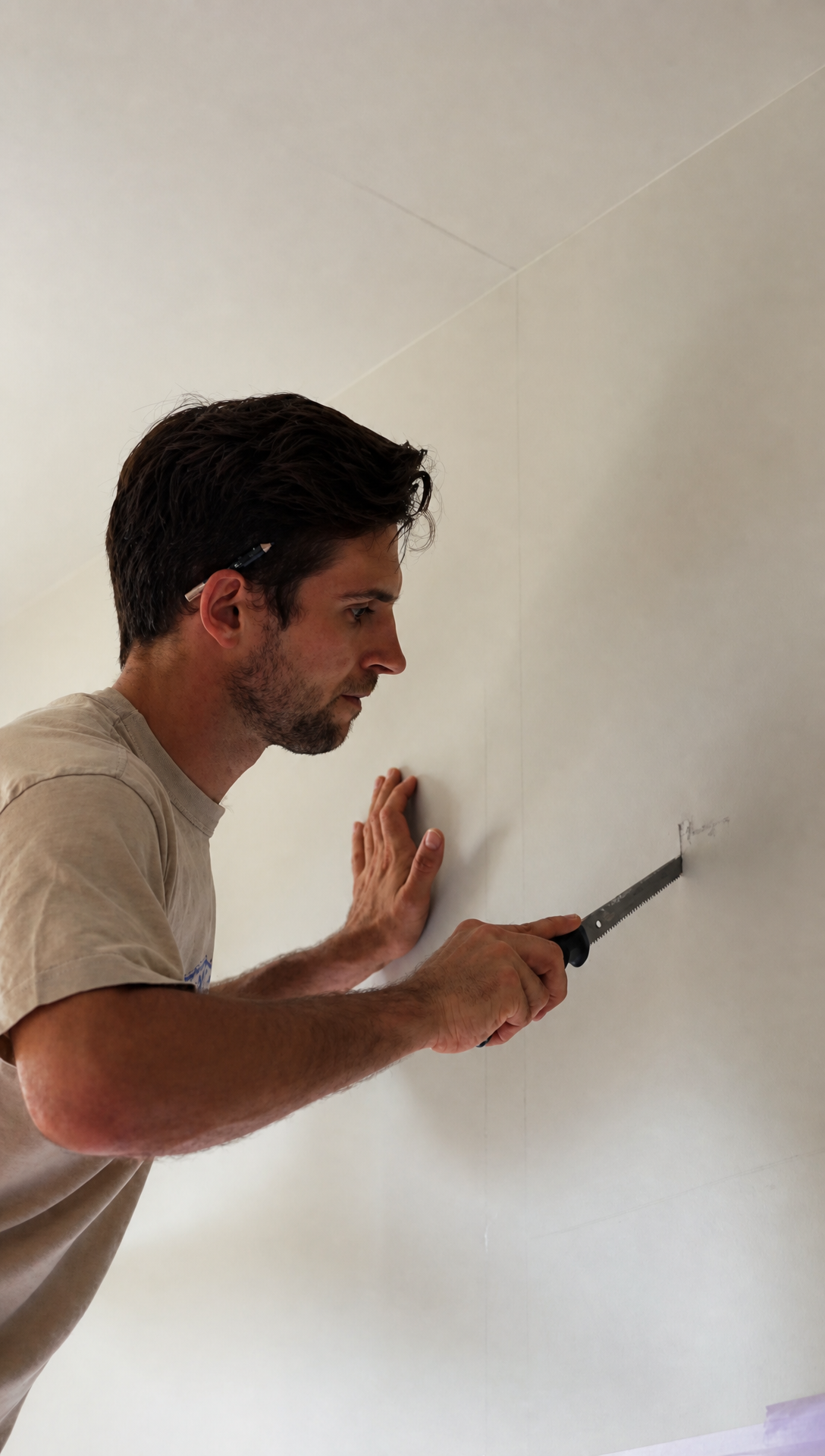 Hugo cutting into the kitchen wall above the stove with a plasterboard hand saw