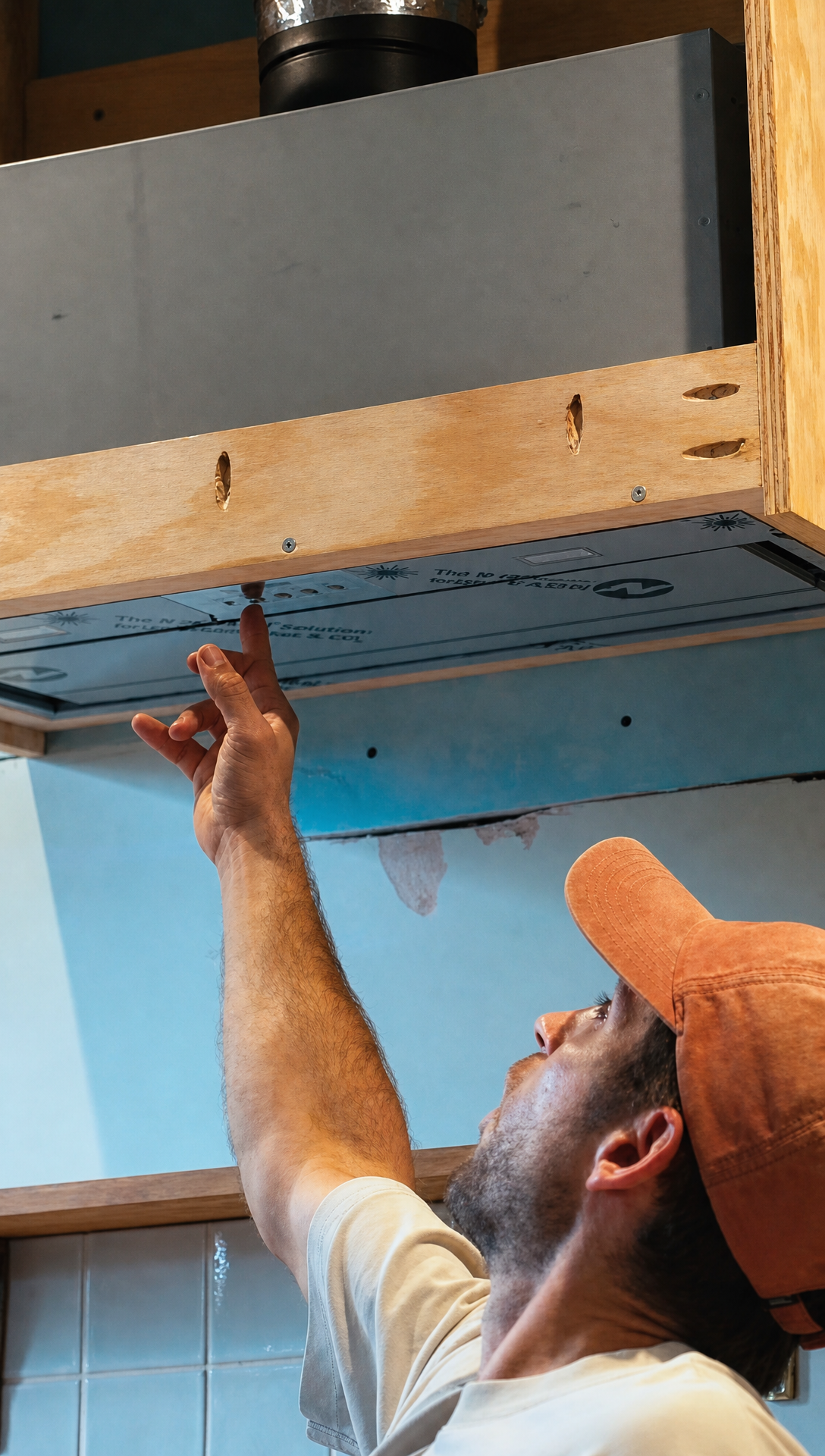 Hugo reaching up to the extractor unit seated in its wall mounted frame above the stove