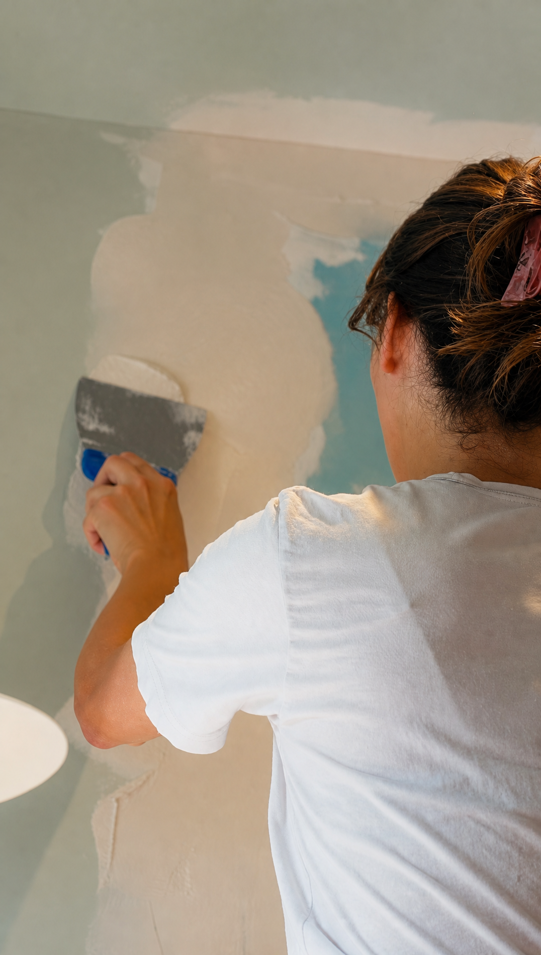 Romy skimming plaster over a taped plasterboard joint beside the hood with a jointing knife