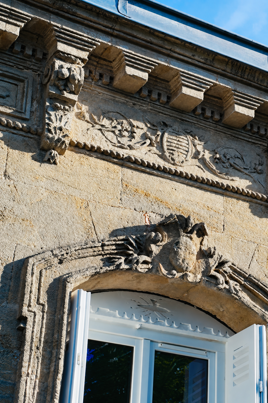 Carved stone detail on the facade of La Chartreuse against a blue early summer sky, framed by leaves