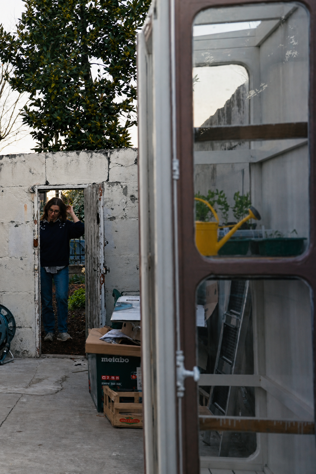 The cluttered covered area between the two gardens, Romy standing in the old narrow doorway with her hand on the frame