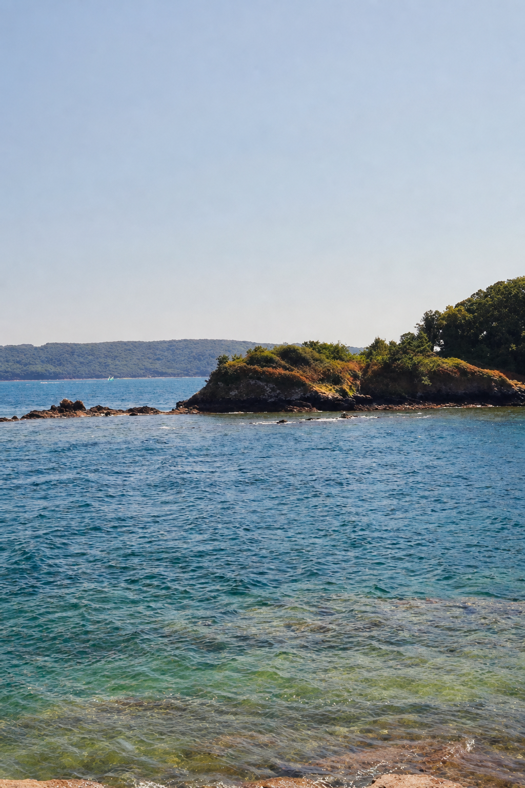 Clear turquoise water in a small cove on the Rade de Brest with a low wooded point behind