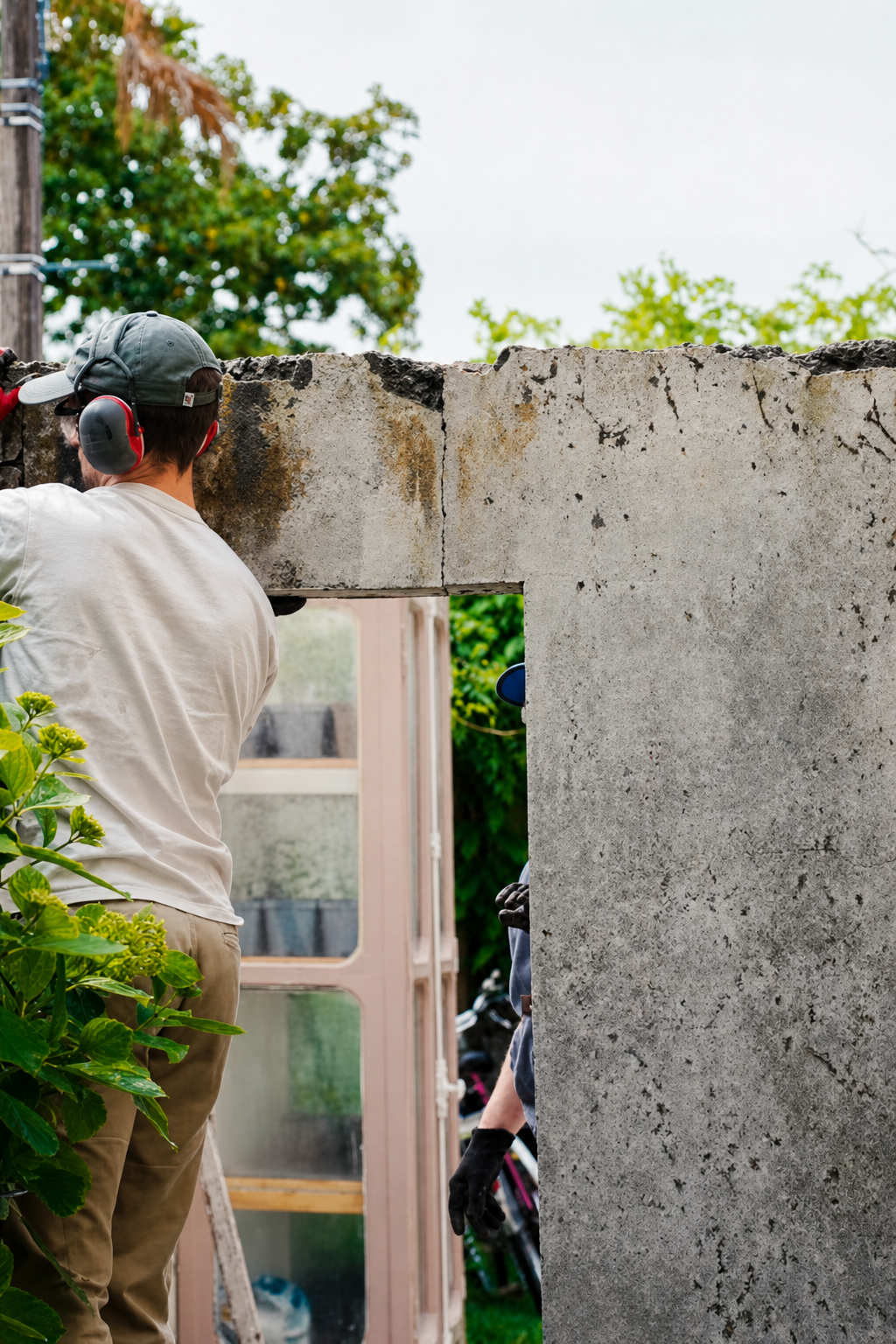 Hugo in cap and ear defenders working at the widened doorway opening, the cut edge of the old wall exposed