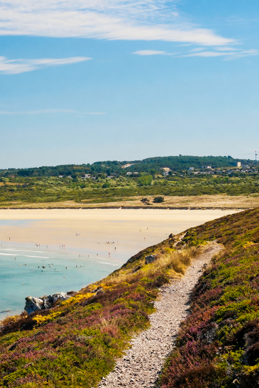 A narrow path through purple heather leading down to a white sand beach and turquoise bay on the Crozon peninsula