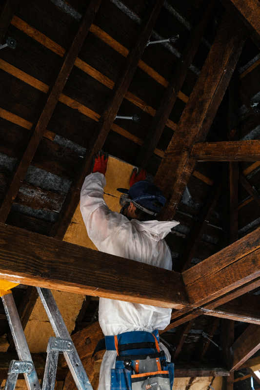 Figure in a dust suit fitting wood fibre insulation between the attic battens