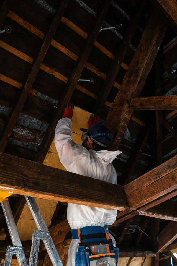 Figure in a dust suit fitting wood fibre insulation between the attic battens