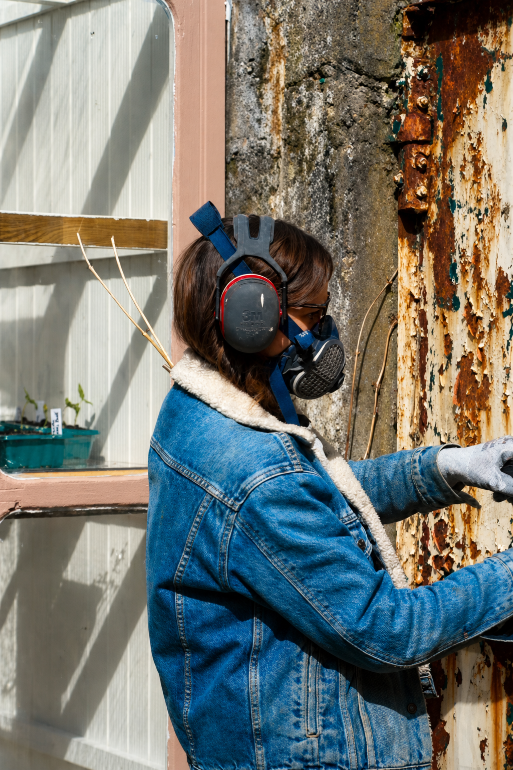 Romy in a respirator and ear defenders sanding the rust off the old garden gate