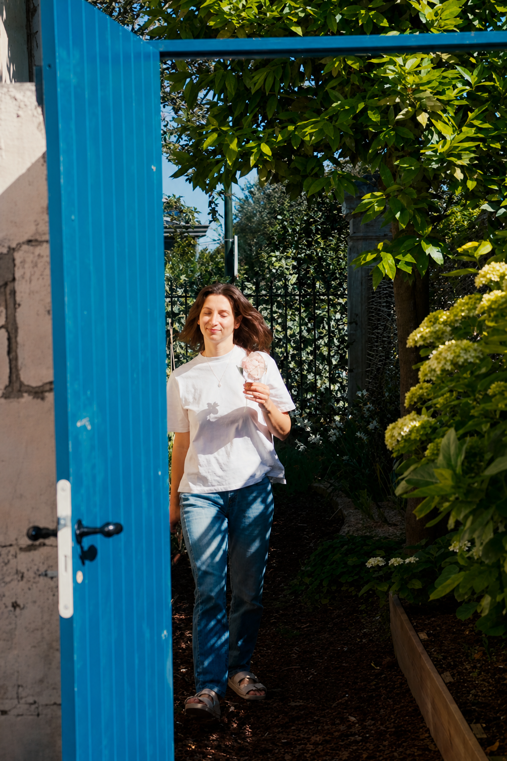 Romy stepping through the newly hung blue garden door with the back garden greenery behind her