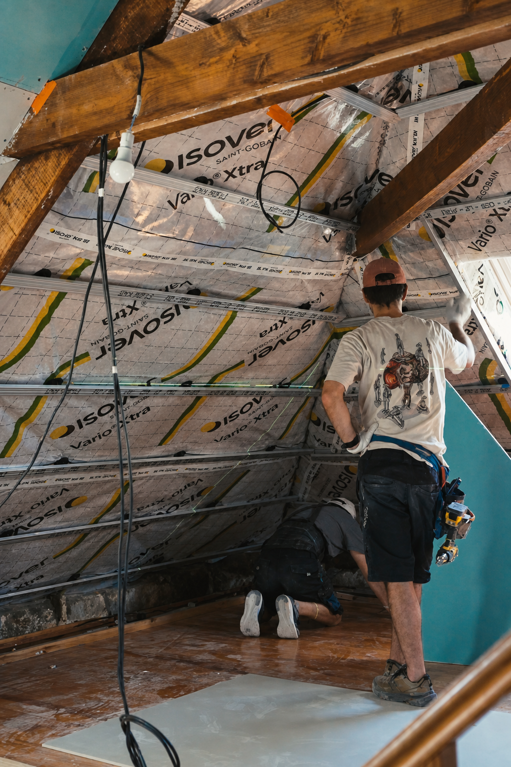 Half boarded attic with blue moisture resistant plasterboard on the sloping ceiling and two people working