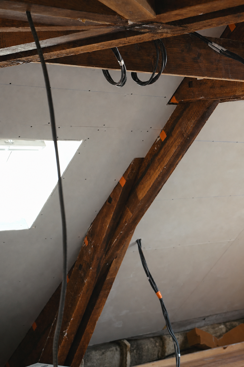 Freshly plasterboarded slopes meeting the exposed oak beams, with electrical cables hanging ready