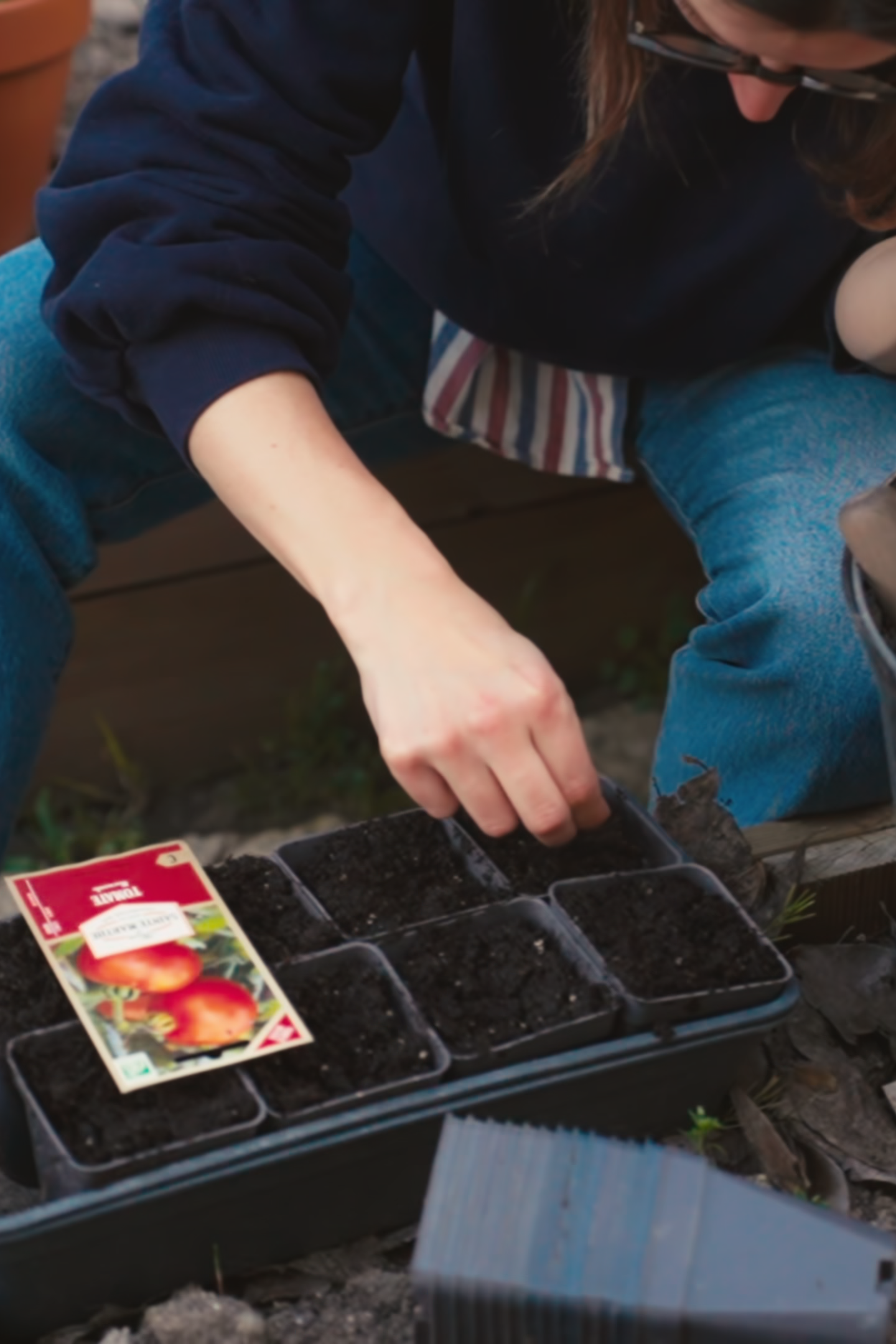 Romy sowing seeds into a module tray beside a bucket of compost