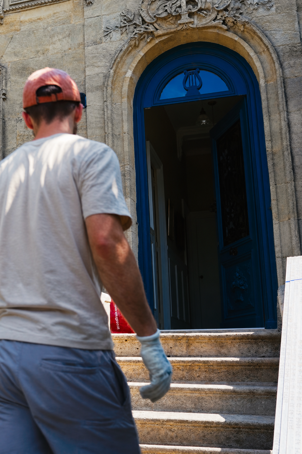 Hugo heading up the front steps toward the open blue door with the delivered framing material stacked to the right