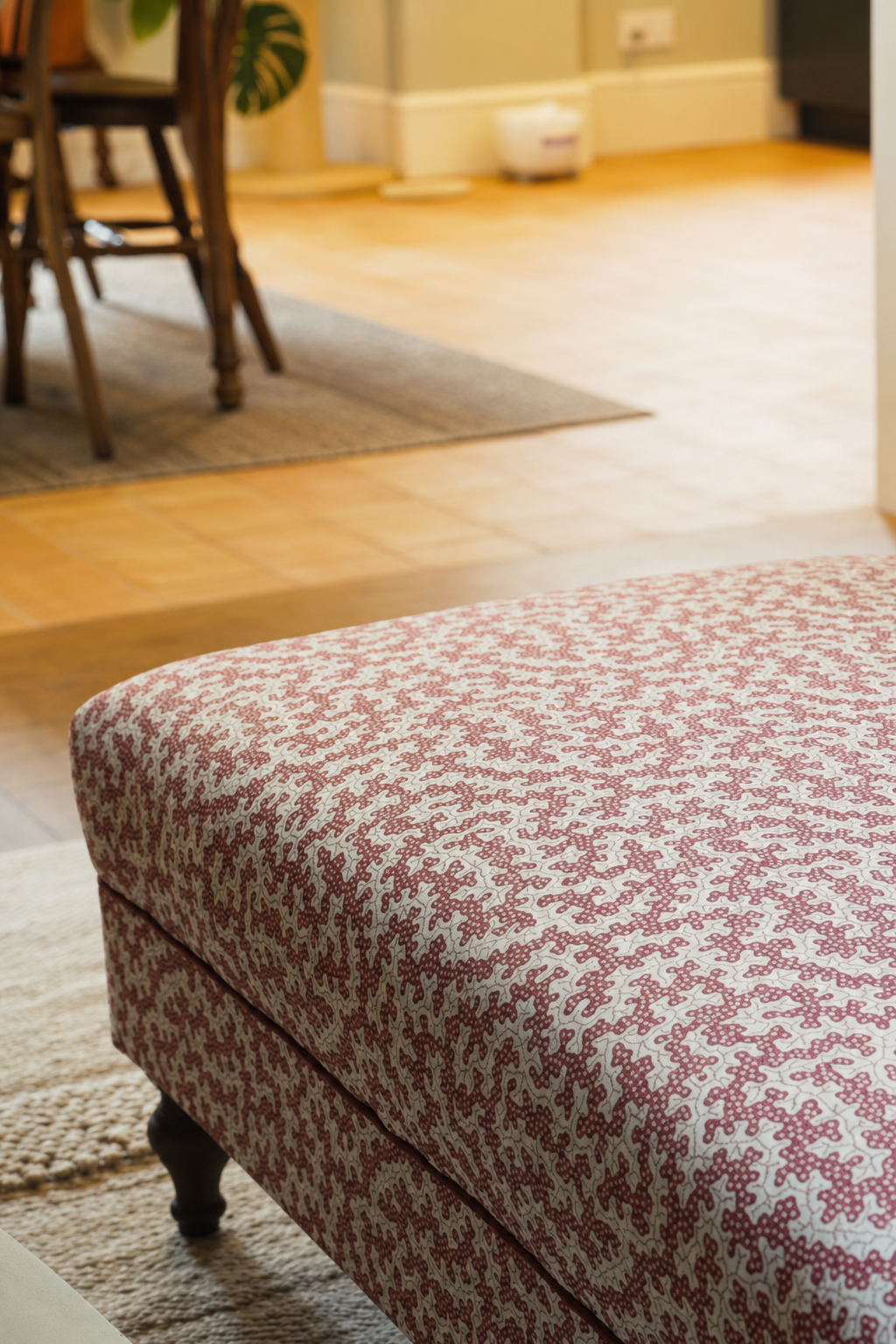 The finished upholstered footstool in the living room with its red and white patterned fabric and the top left corner in view