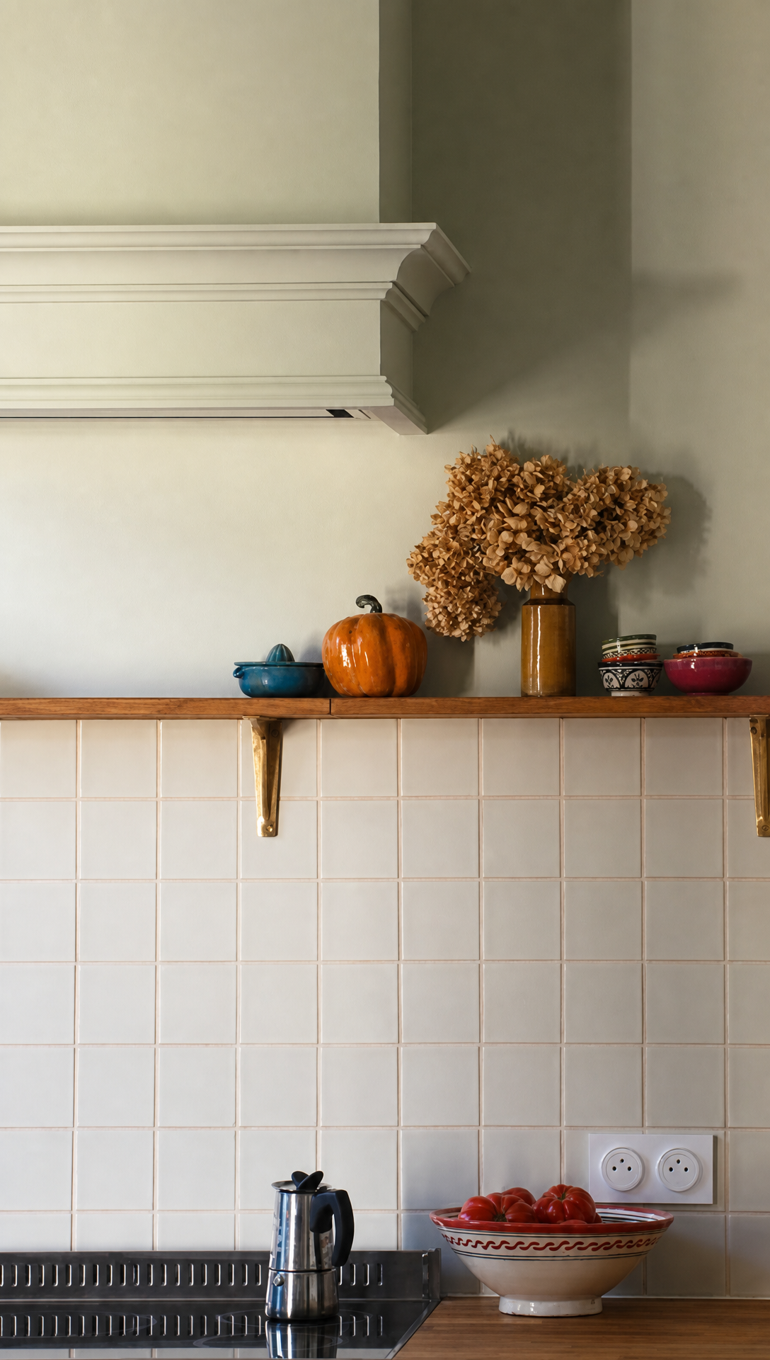 The finished range hood above the shelf, dressed with a dried hydrangea, a pumpkin and a bowl of tomatoes