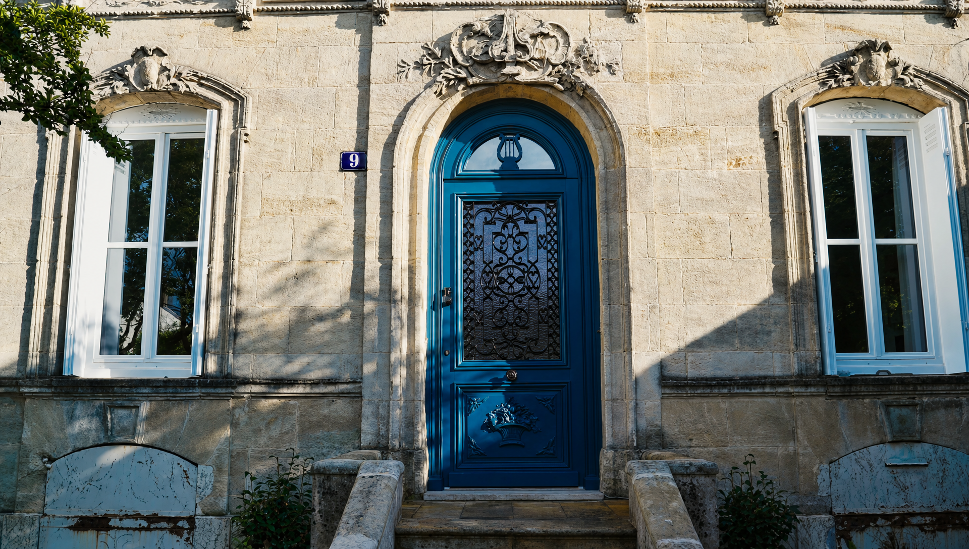 The symmetrical stone facade of the house with the blue arched front door, two tall windows and steps up to the entrance