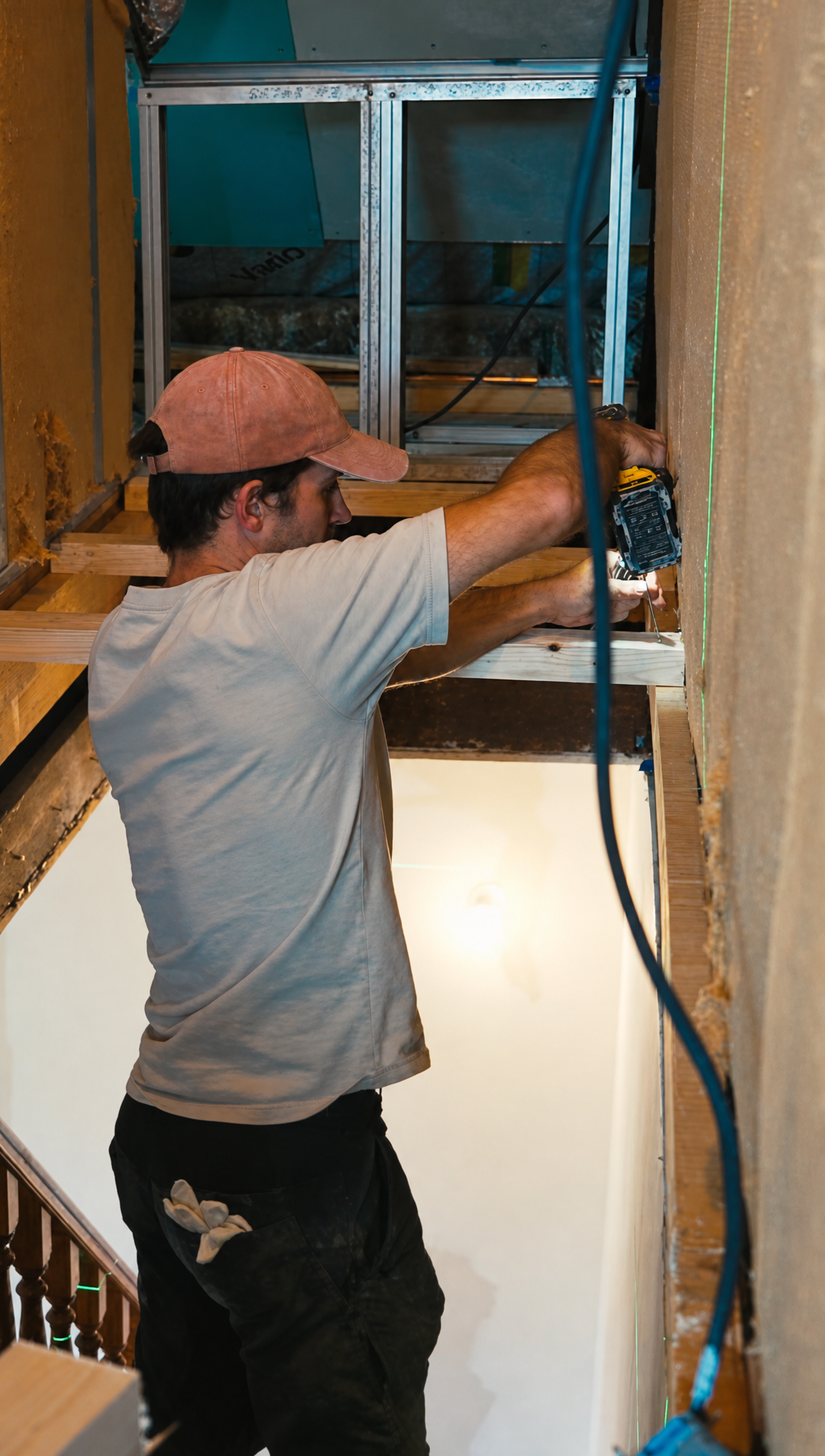 Hugo fixing lengths of timber across the open stairwell with a drill to make a working platform