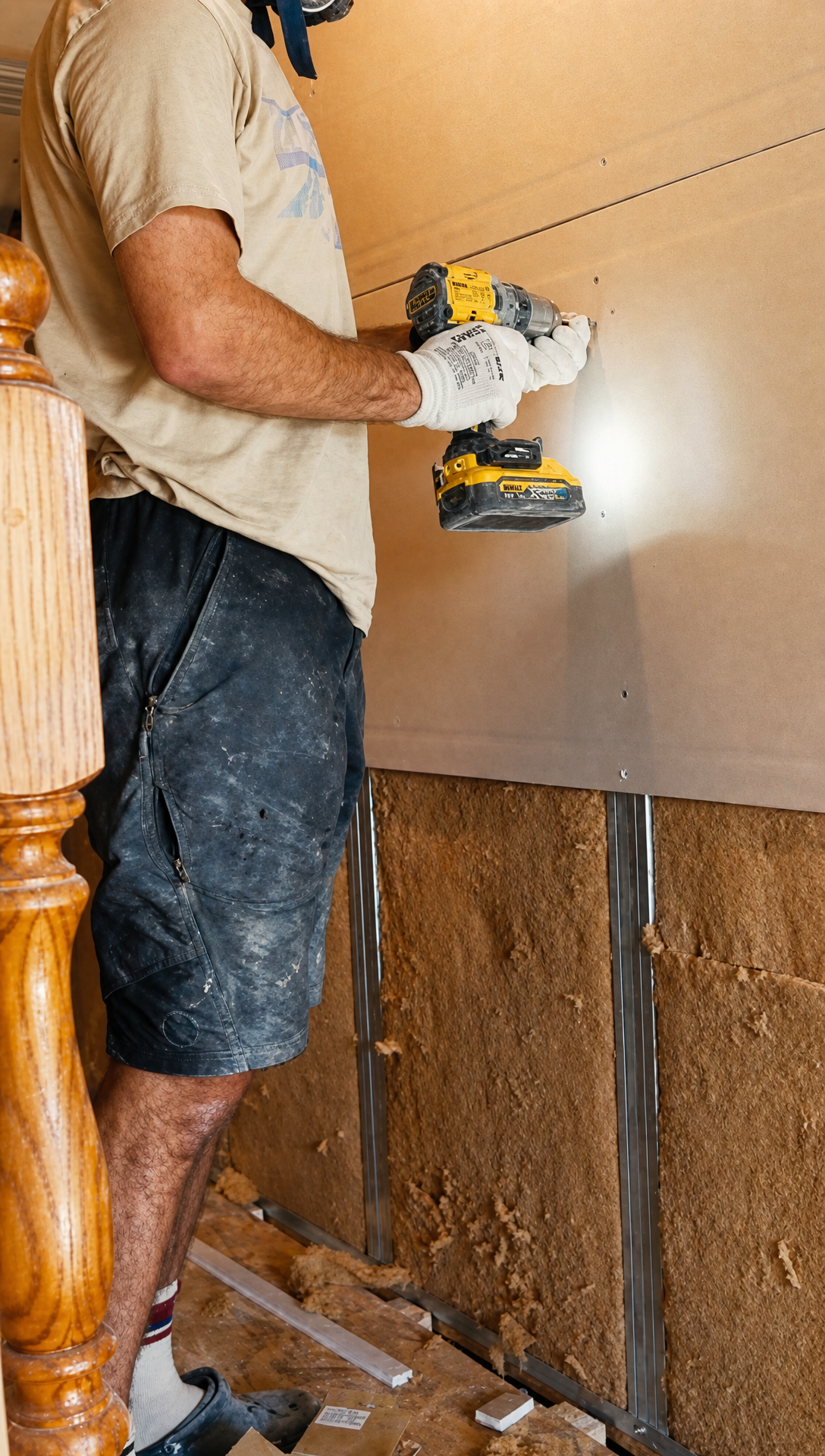 Hugo screwing a sheet of plasterboard to the wall above the stair banister, insulation still showing below it