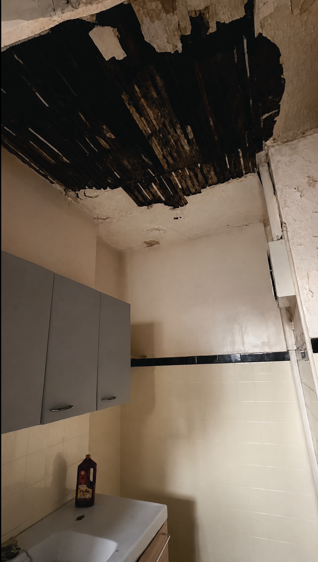 A hole in the kitchen ceiling exposing blackened timber, above the old kitchen units
