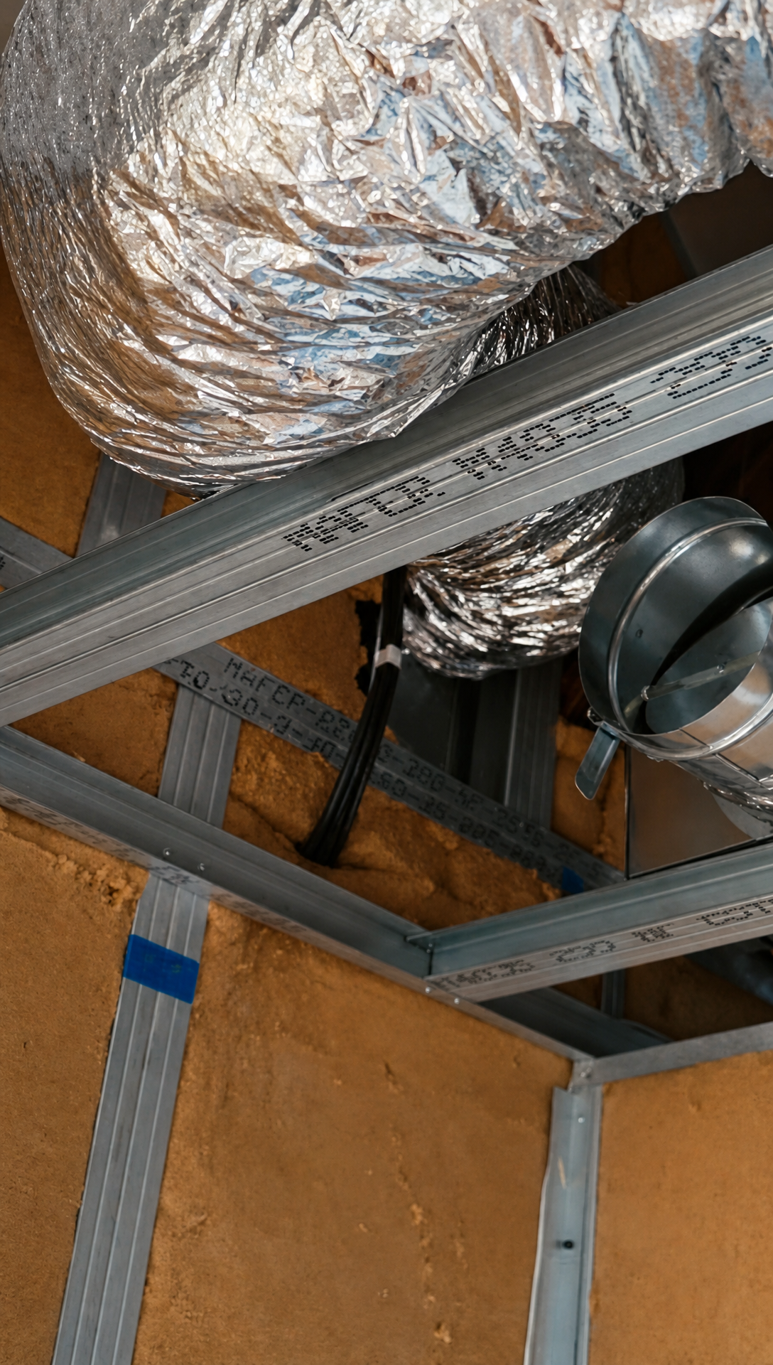 Silver flexible aircon ducting running through the metal ceiling frame above the insulated walls
