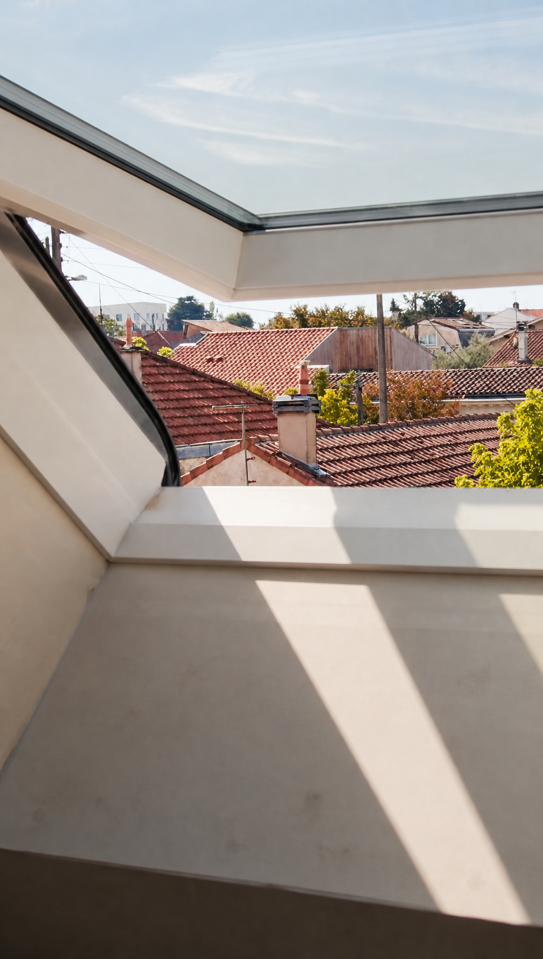 View through an open roof window across terracotta rooftops, with sunlight falling on the newly boarded window reveal