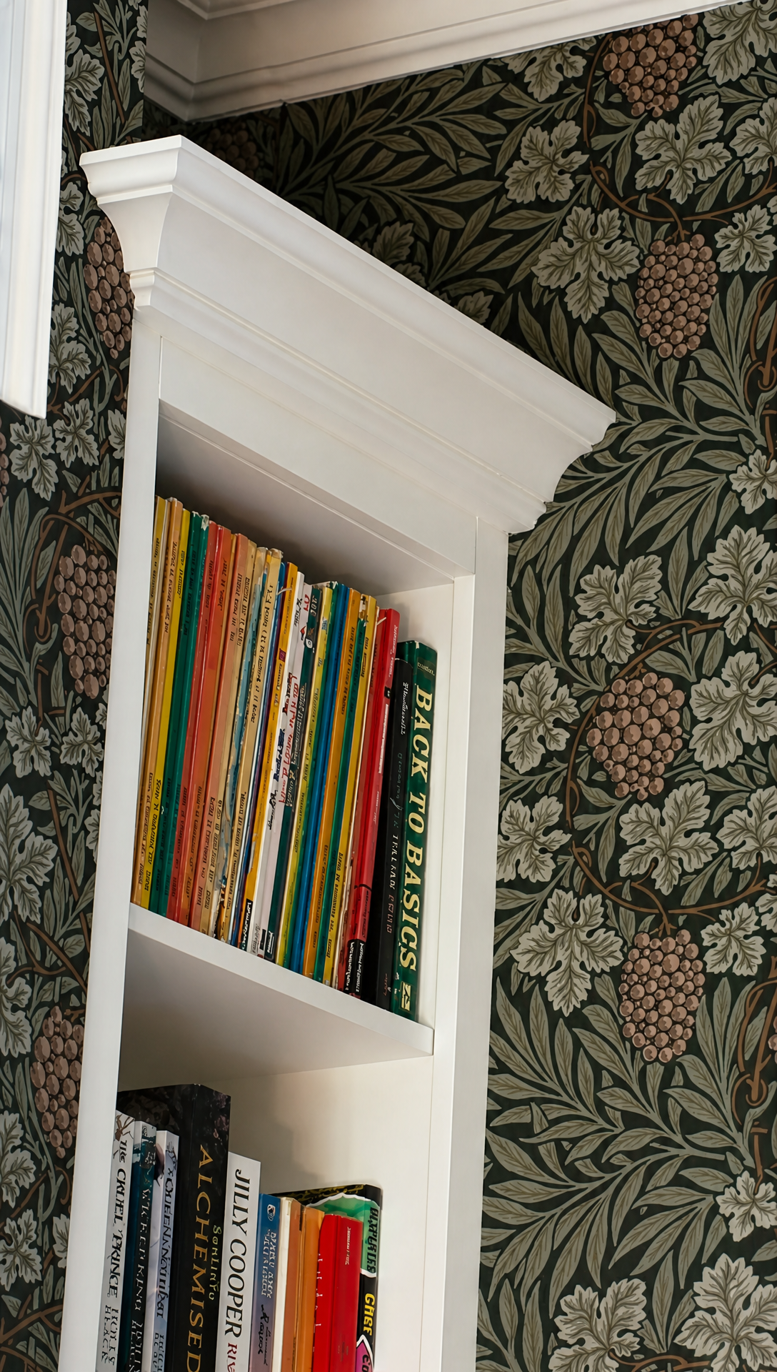 Tall white built-in bookcase full of books against dark green William Morris Vine wallpaper