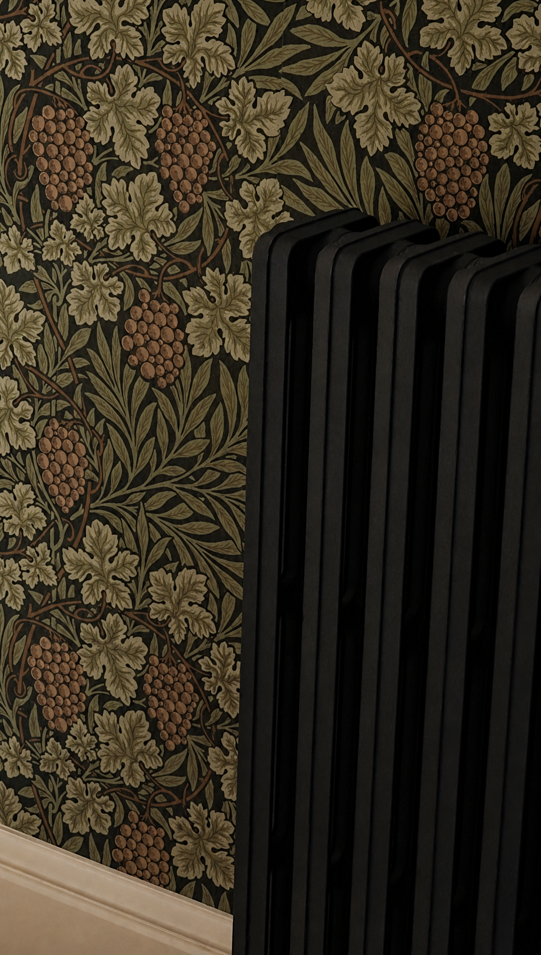 An original cast iron radiator painted black against the Vine wallpaper