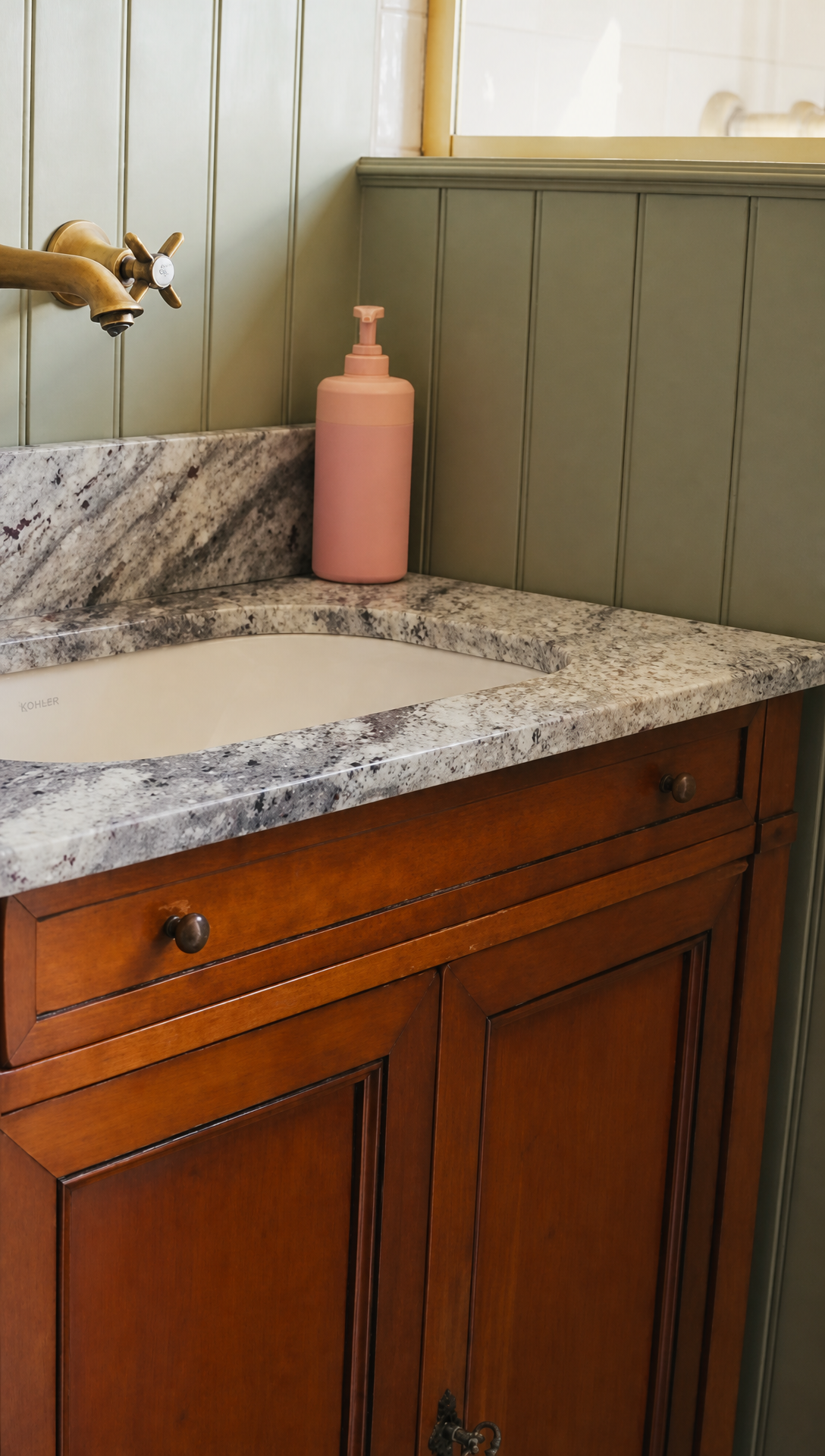 An antique wooden vanity with a grey granite top, an inset basin and wall mounted brass taps