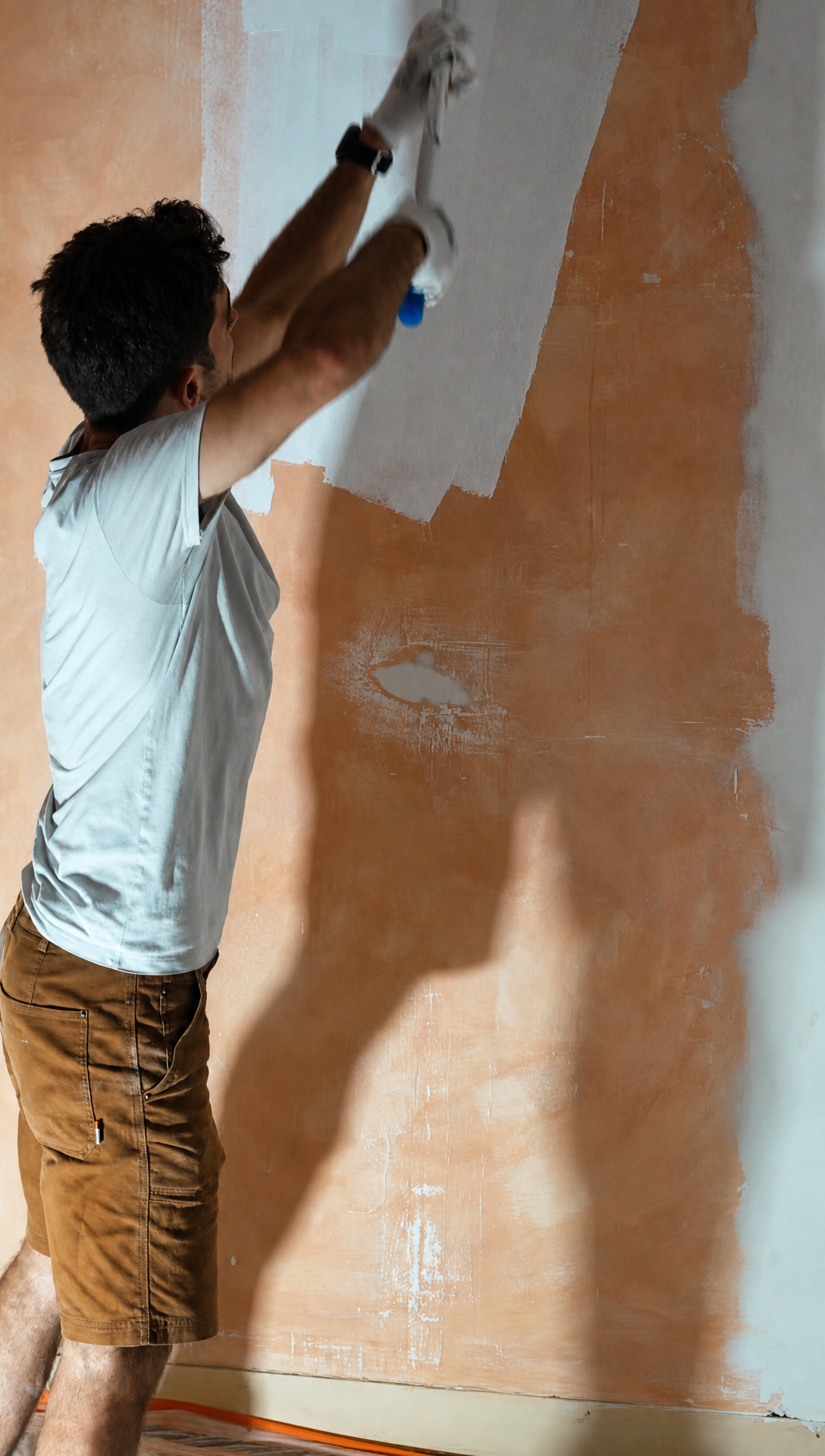 Hugo rolling white paint onto a bare orange plaster wall in the bedroom