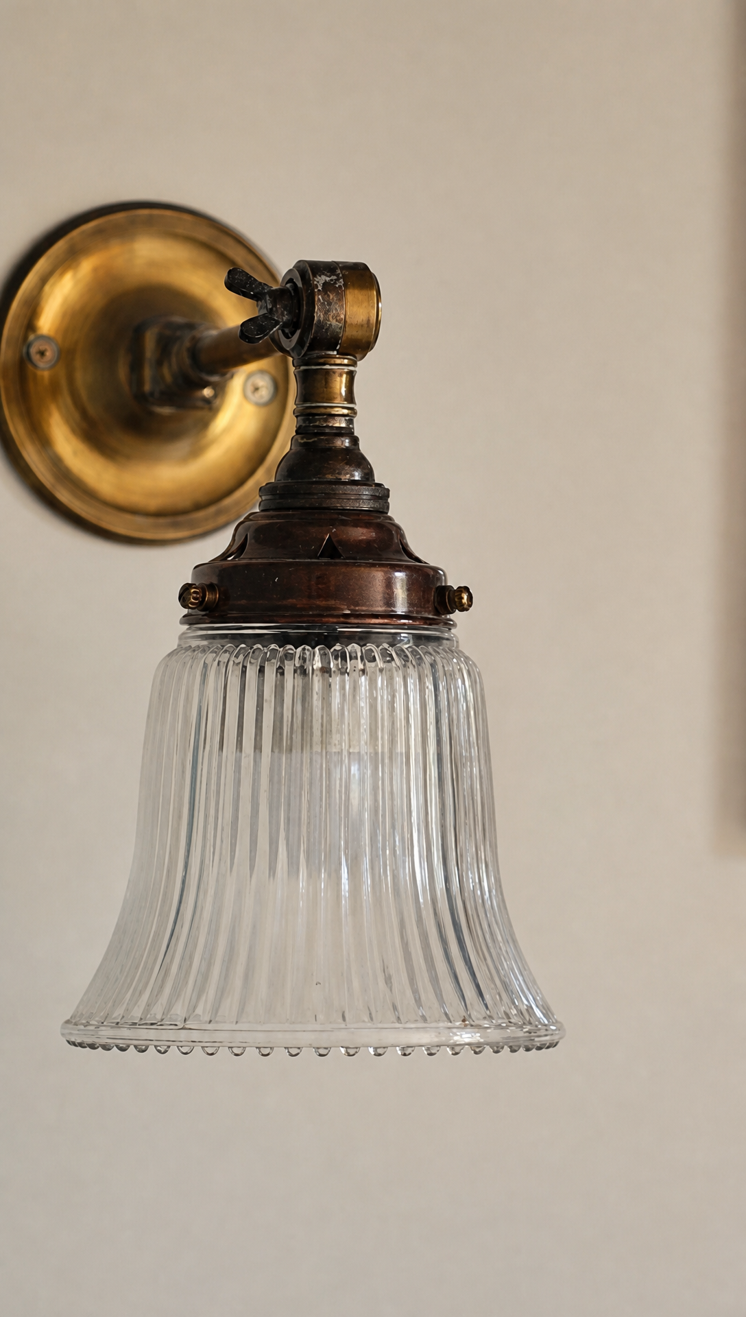 A brass wall light with a fluted glass shade on a pale wall