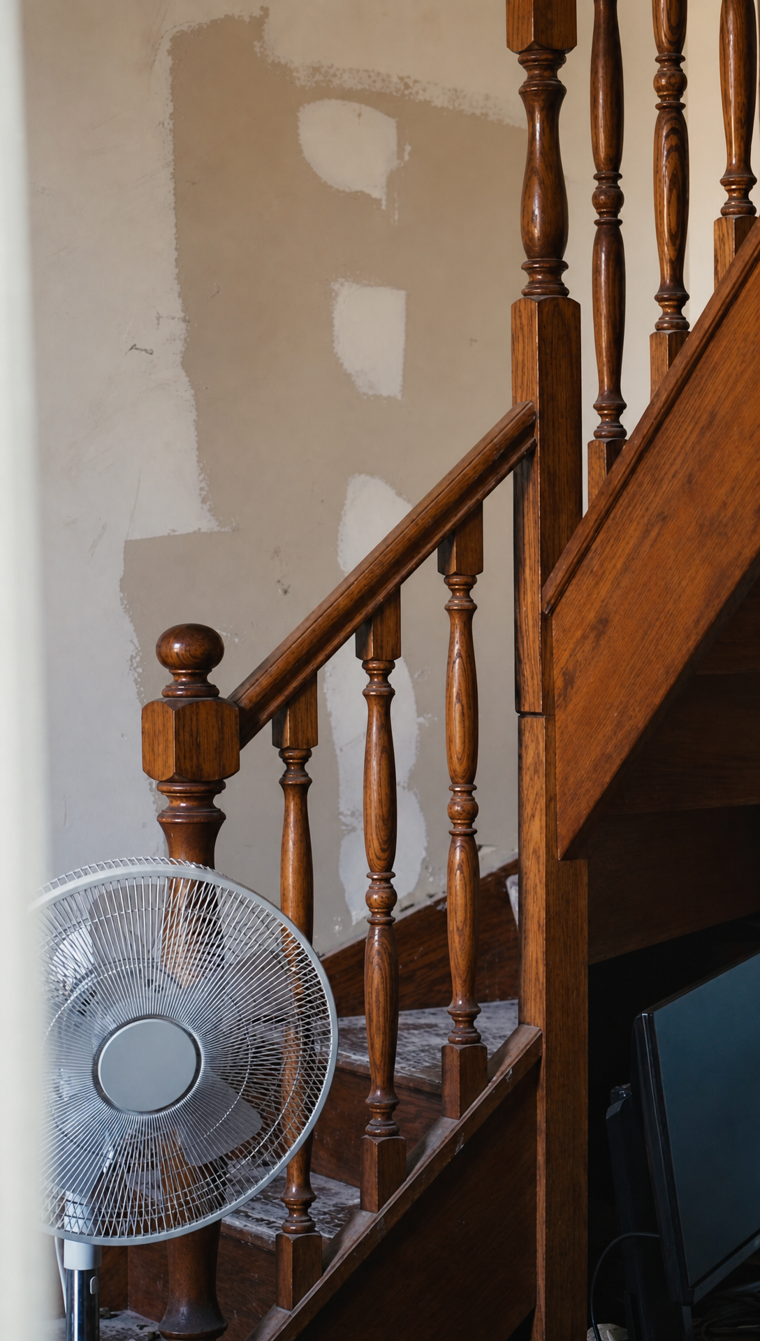 The unfinished office with patched plaster walls, the wooden staircase and two fans on the floor